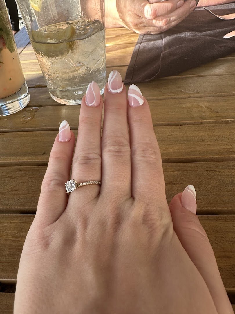 Manicured hands beside polish bottles.